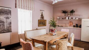 A dining area with a wooden table and chairs, a ceiling fan, and a kitchen in the background.