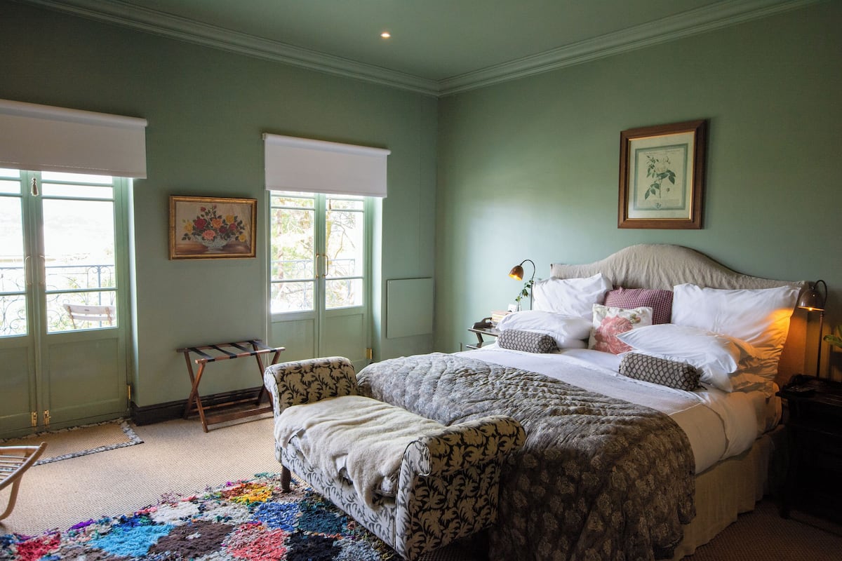 A bedroom with a large bed, a bedside table with a lamp, a chair, and a colorful rug.
