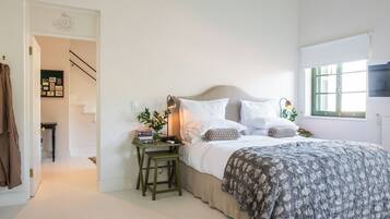 A bedroom with a bed, bedside tables, a nightstand, a window with blinds, and a staircase leading to another room.