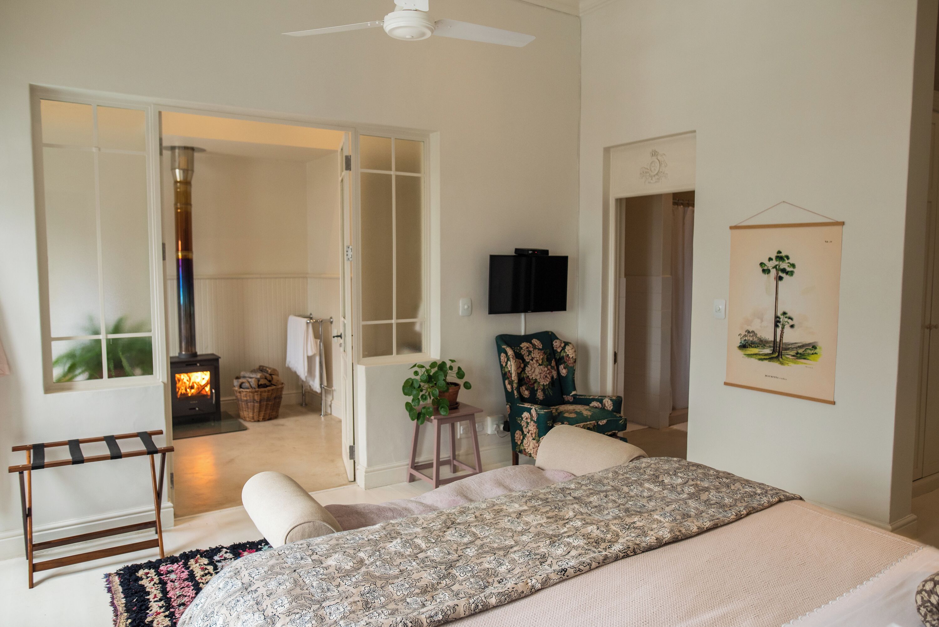 A bedroom with a bed, a chair, a television, a fireplace, and a door leading to another room.