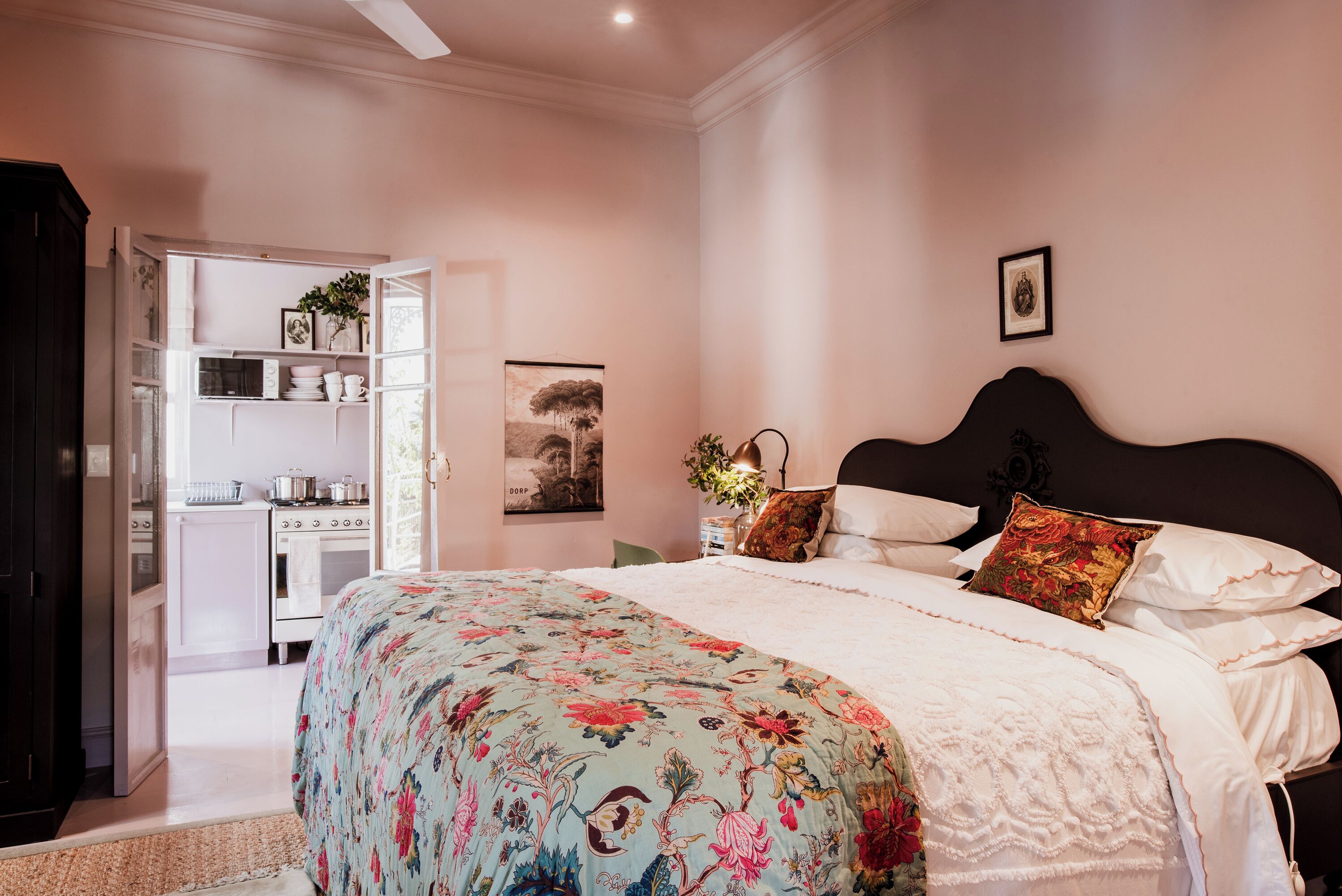 A bedroom with a large bed, a nightstand, a dresser, and a view of a kitchen.