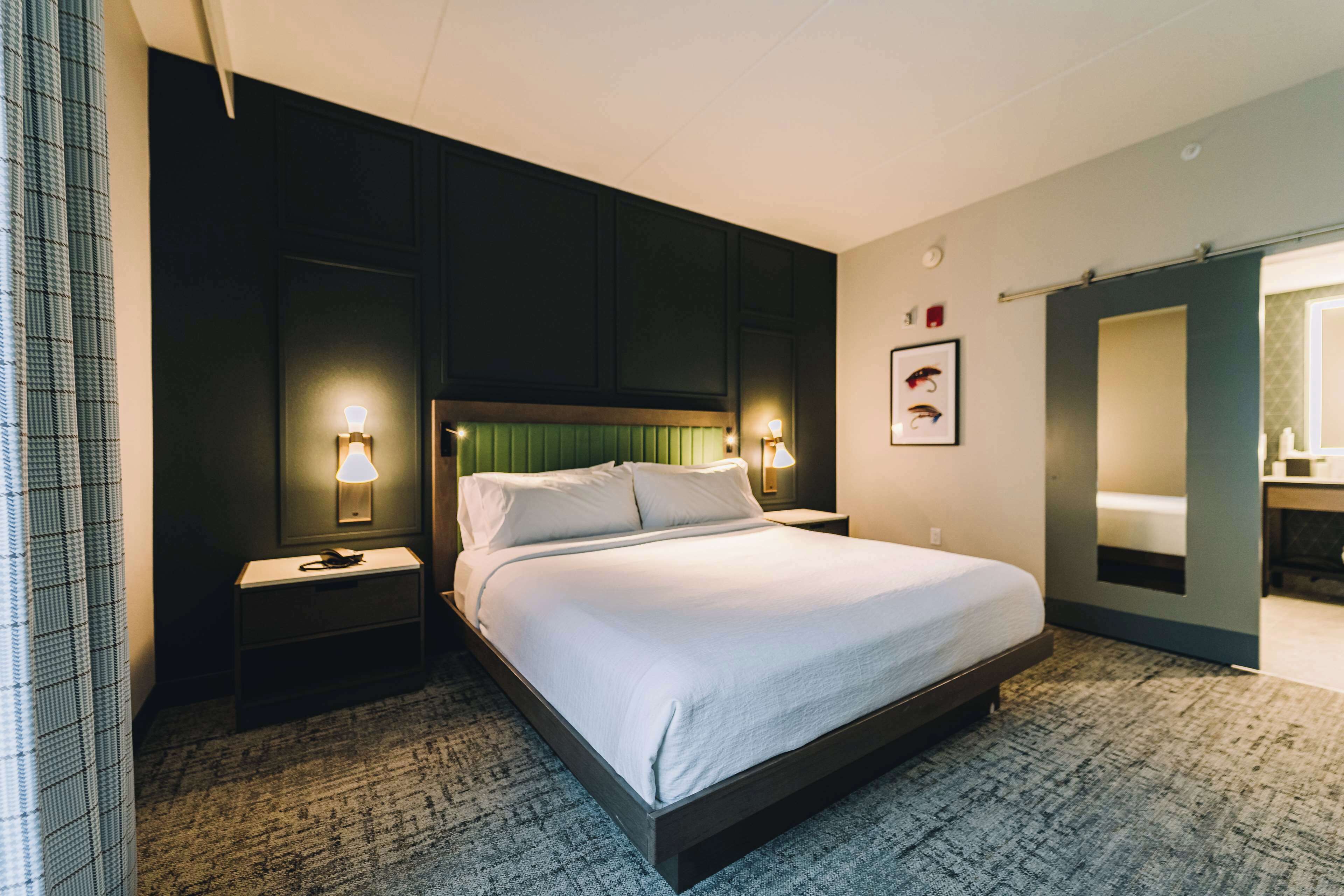 A hotel room with a large bed, two bedside tables, a nightstand, a mirror, and a door leading to a bathroom.