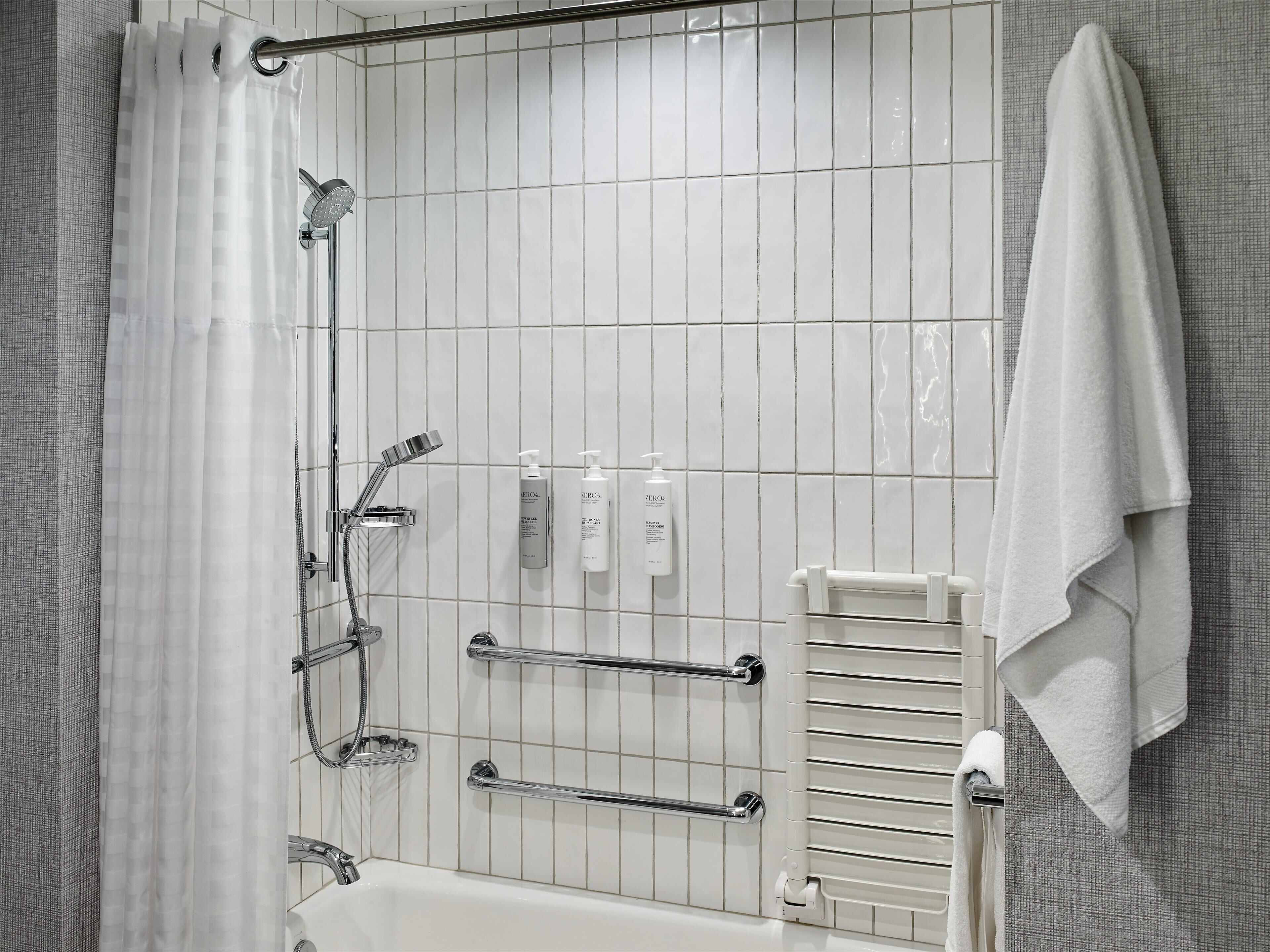 A modern bathroom with a shower, grab bars, a towel rack, and toiletries.