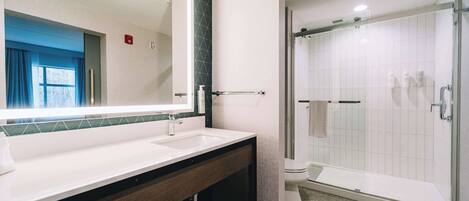 A modern bathroom with a large mirror, two sinks, a shower, and a toilet.