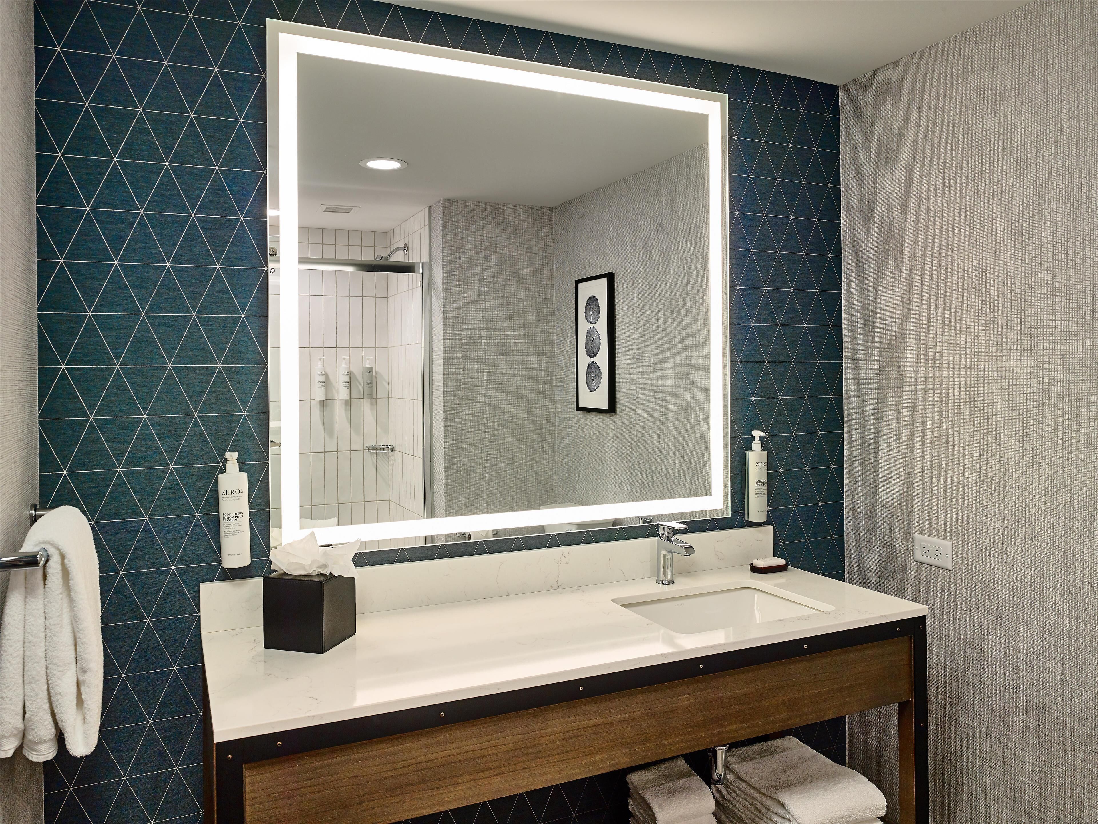 A modern bathroom with a large mirror, white sink, and dark blue patterned walls.