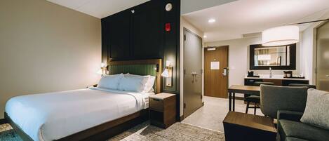 A hotel room with a large bed, bedside tables, a desk, a chair, and a mirror.