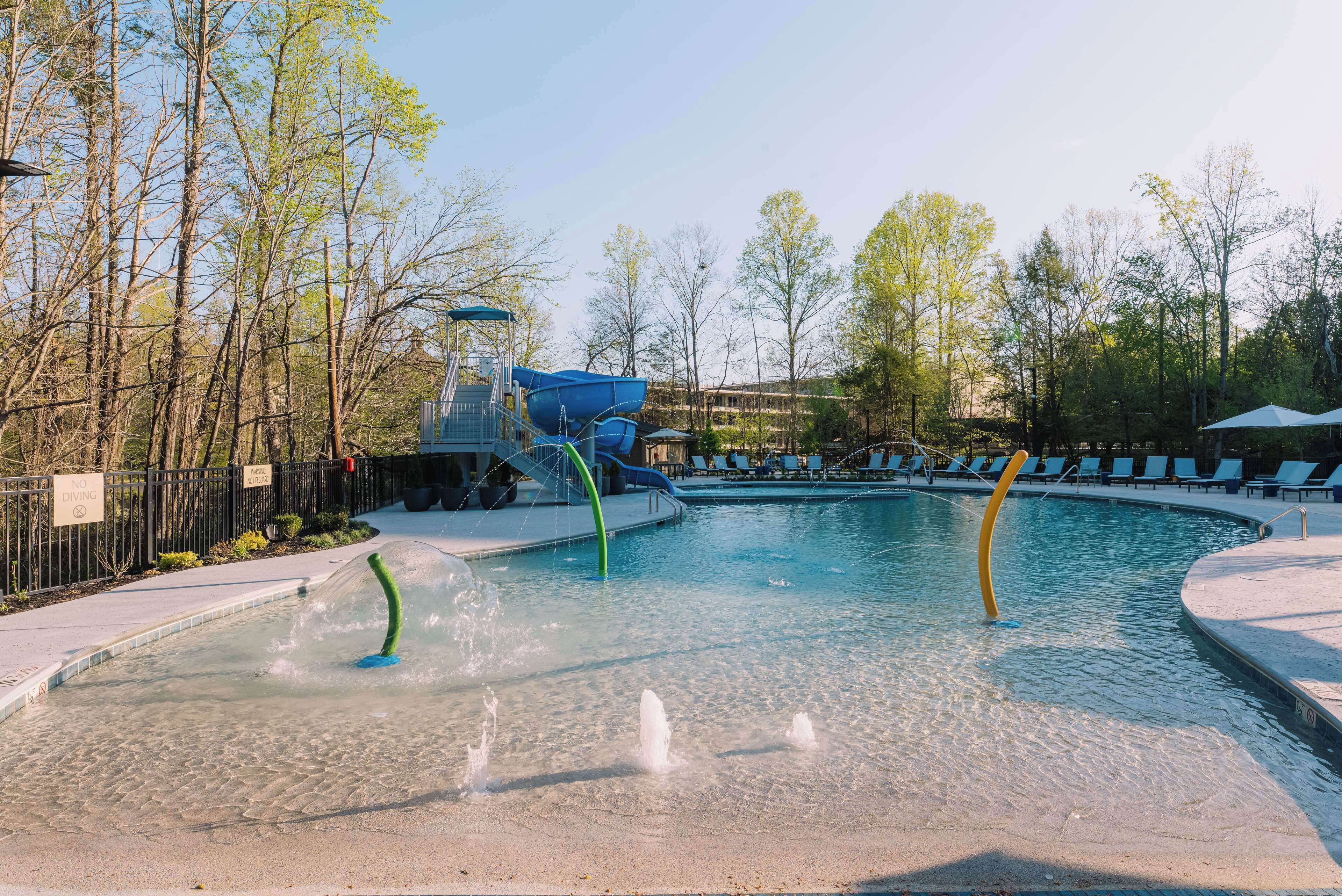 Une piscine avec un toboggan, entourée d’arbres et de chaises longues.