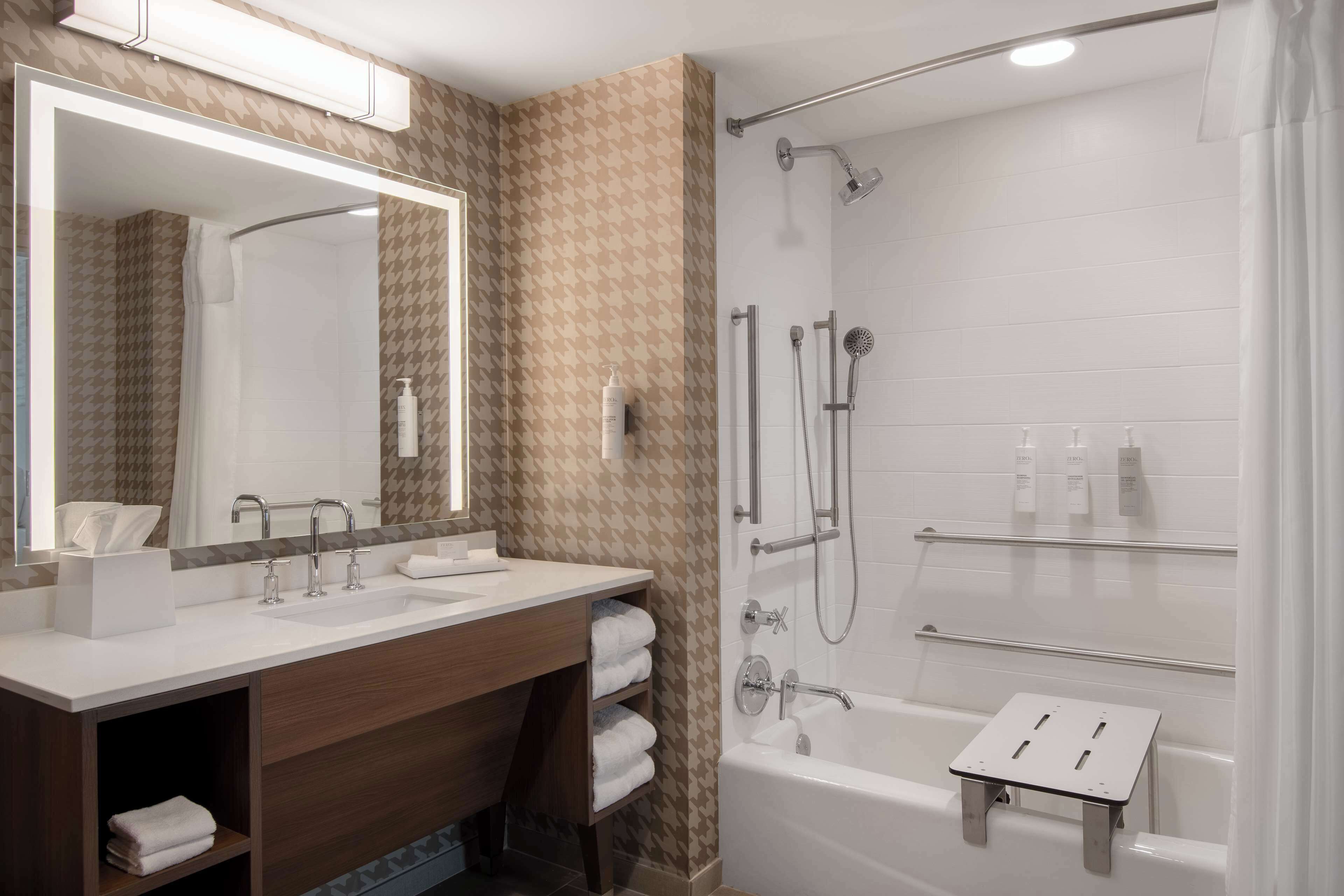 Un baño moderno con tocador de doble lavabo, un espejo grande, ducha con cabezal de ducha manual y bañera con un estante pequeño.