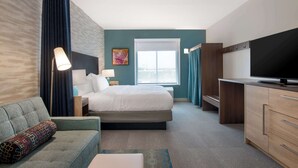 A hotel room with a bed, a sofa, a desk, a TV, and a window.