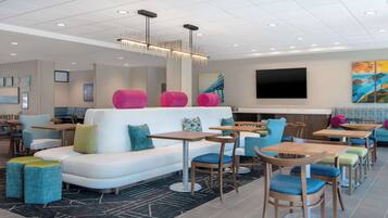 A modern hotel lobby with a white sofa, blue and green cushioned ottomans, wooden tables, and chairs.