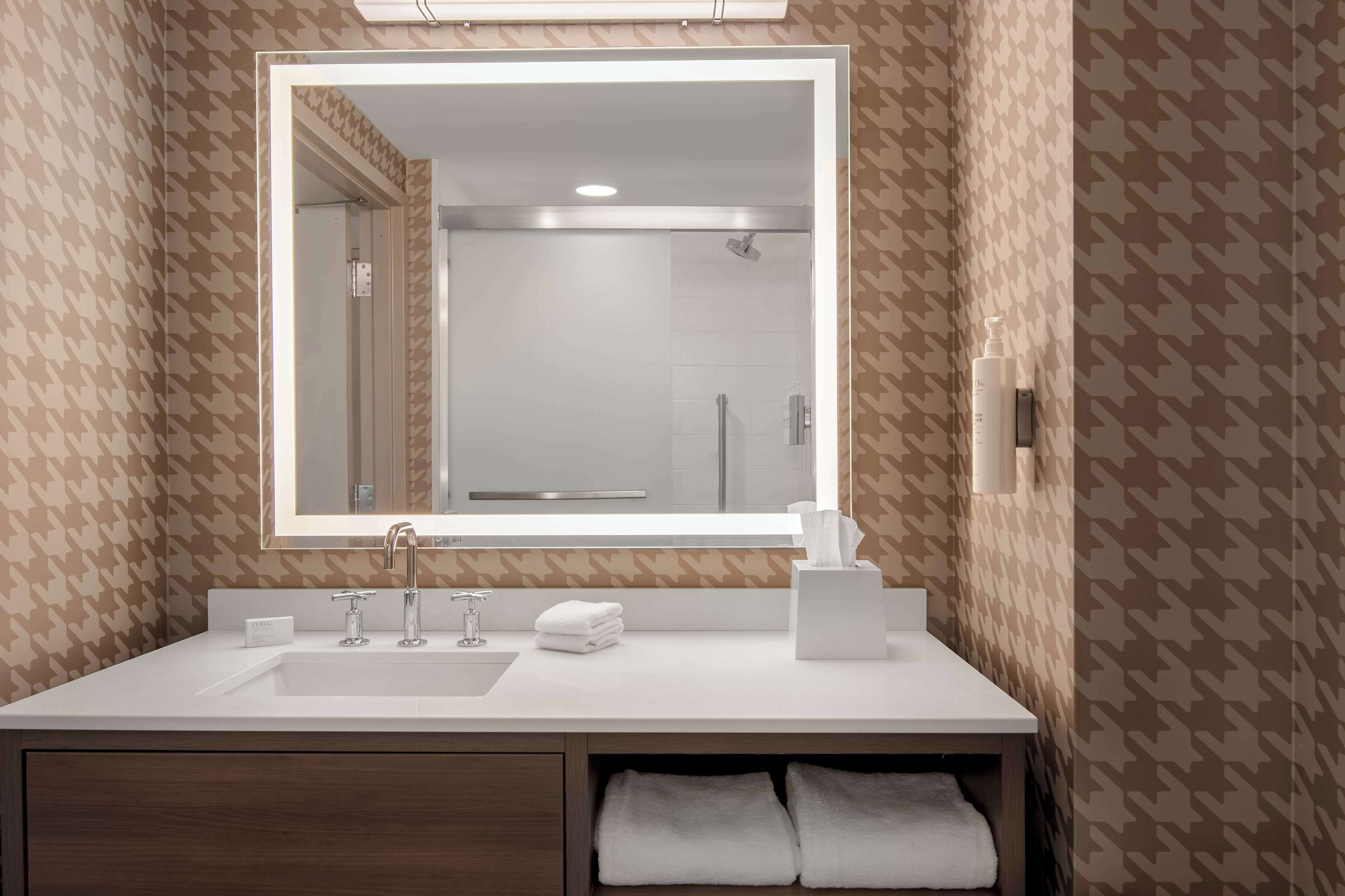 A bathroom with a large mirror, white sink, and towel storage.
