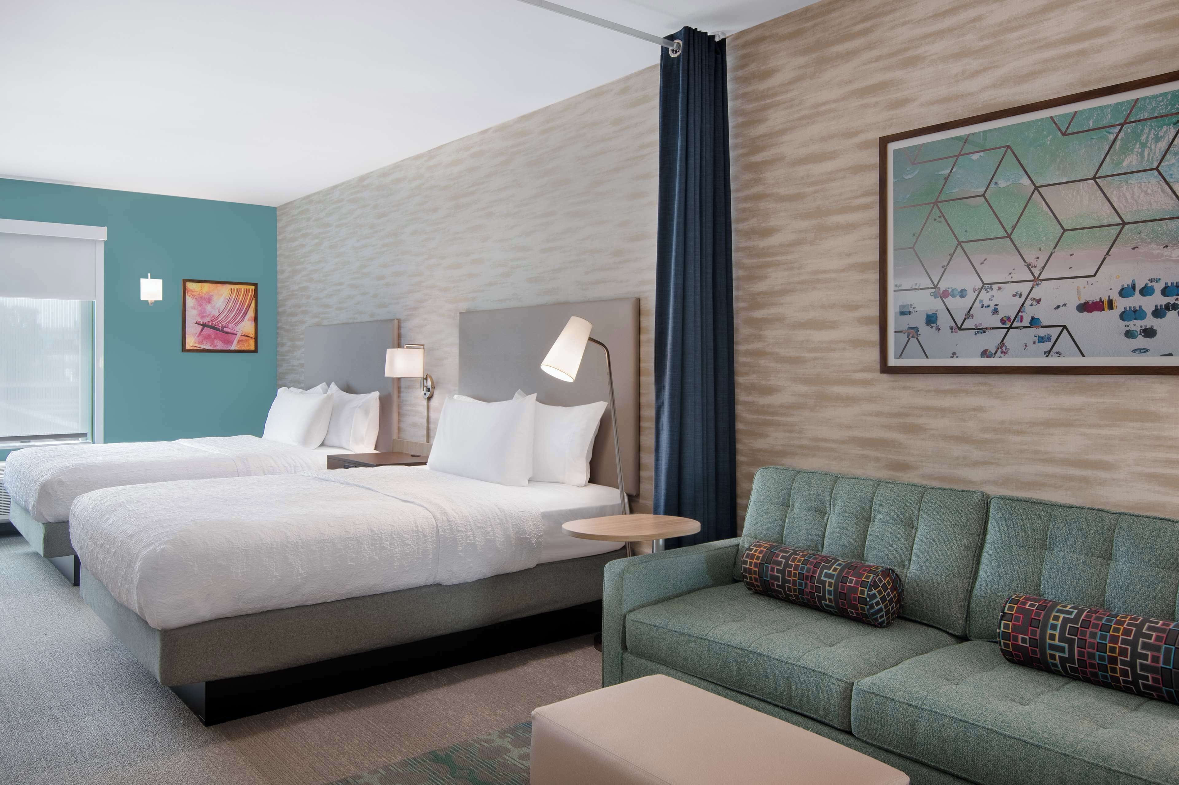A hotel room with two beds, a green sofa, a small round table, and a large abstract painting on the wall.