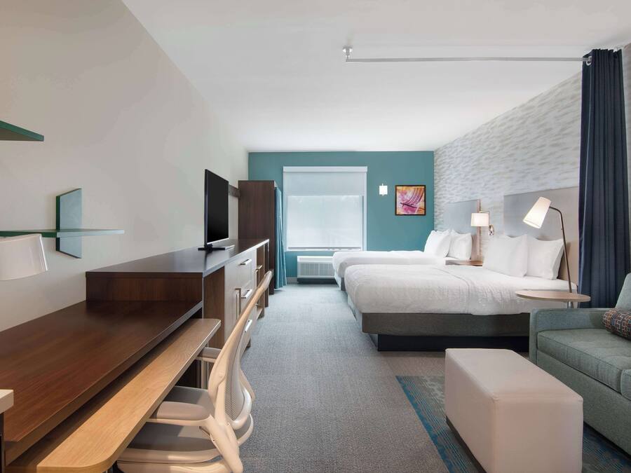 Quarto de hotel moderno com cama, escrivaninha, cadeira e um pequeno sofá.