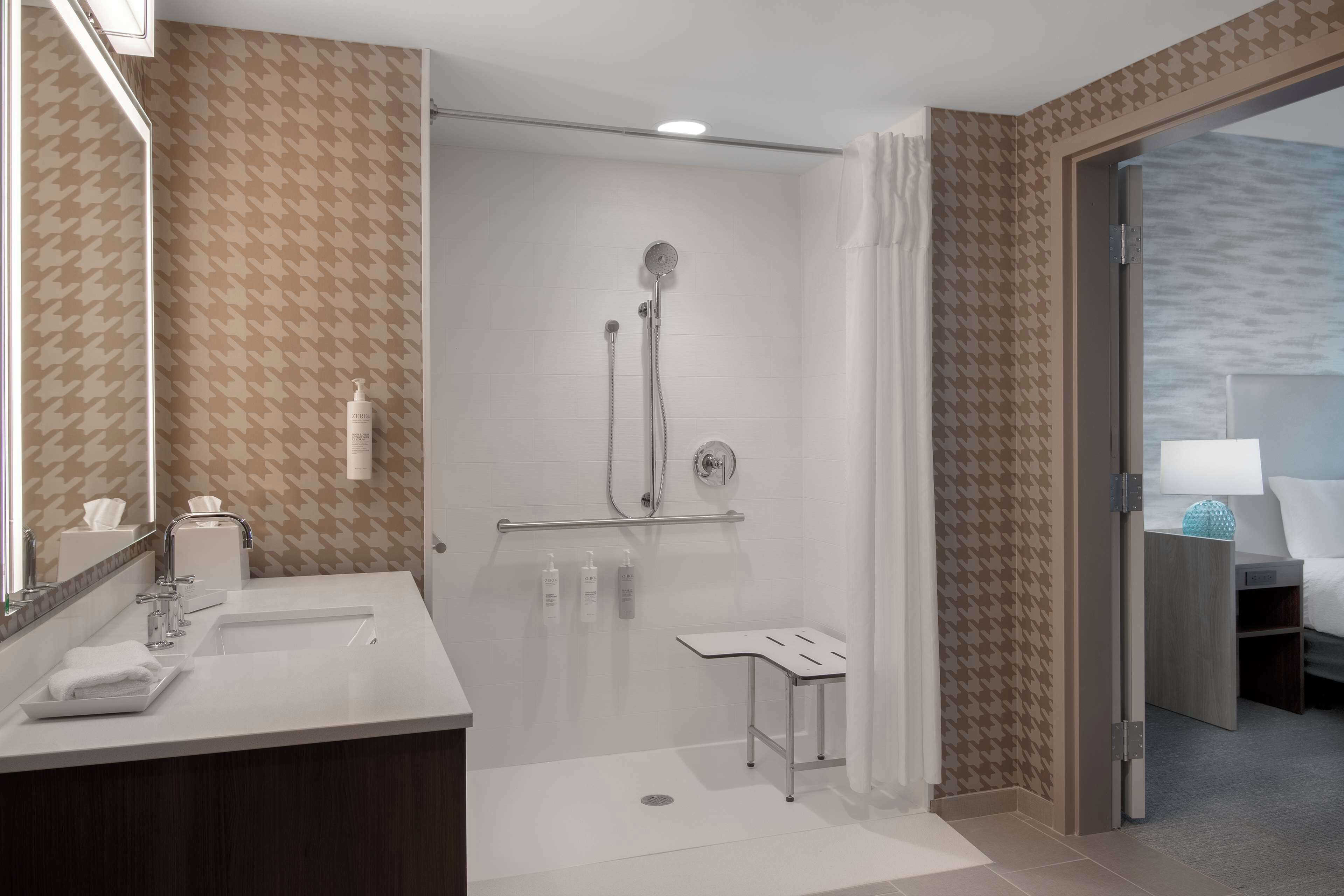 Uma casa de banho moderna com chuveiro, toucador com espelho e mesa de cabeceira.