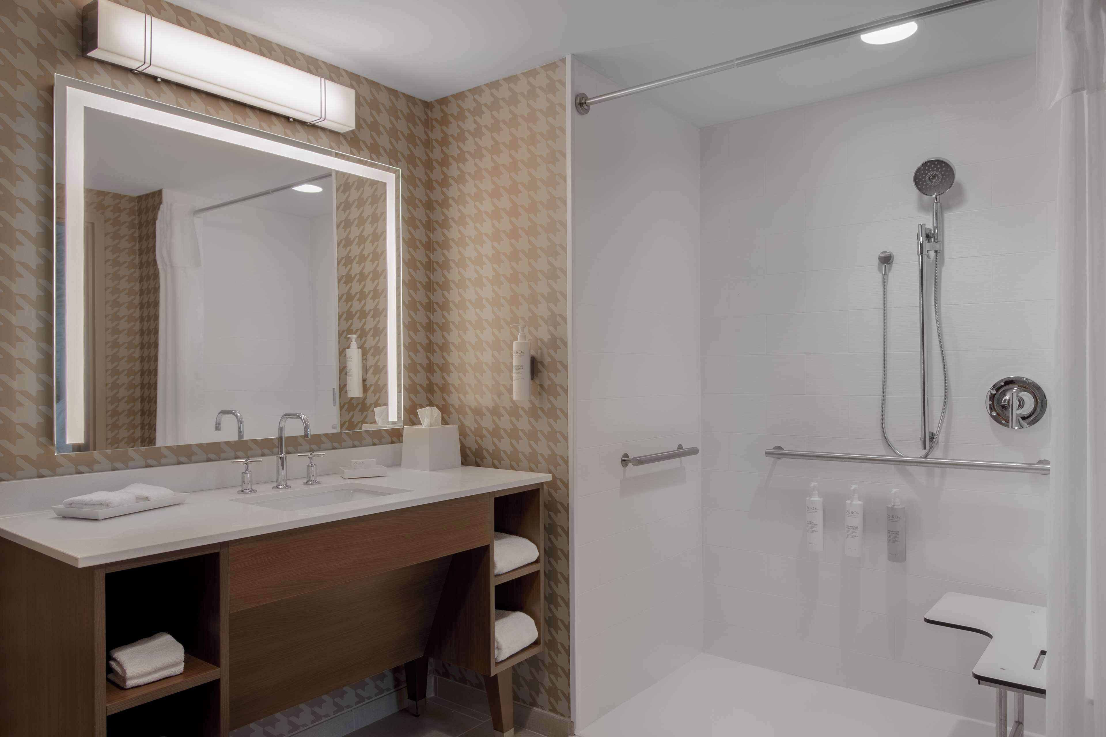 Un baño moderno con un espejo grande, una ducha con puerta de cristal y un tocador con lavabo y espacio para toallas.