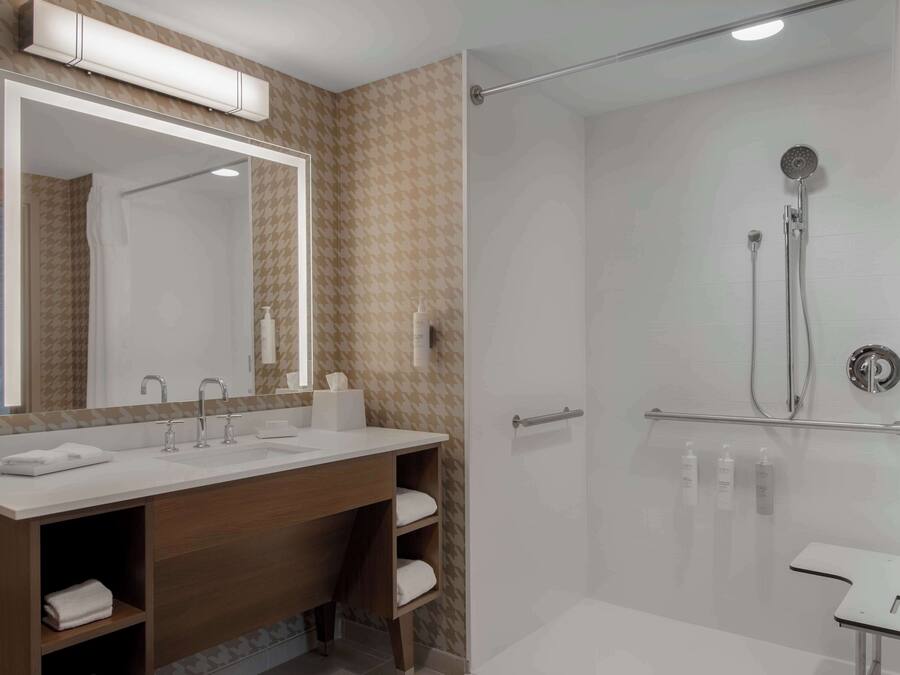 A modern bathroom with a large mirror, a shower with a glass door, and a vanity with a sink and towel storage.