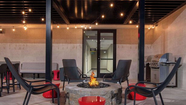 An outdoor patio with a stone fire pit, black chairs, and a red bowl.