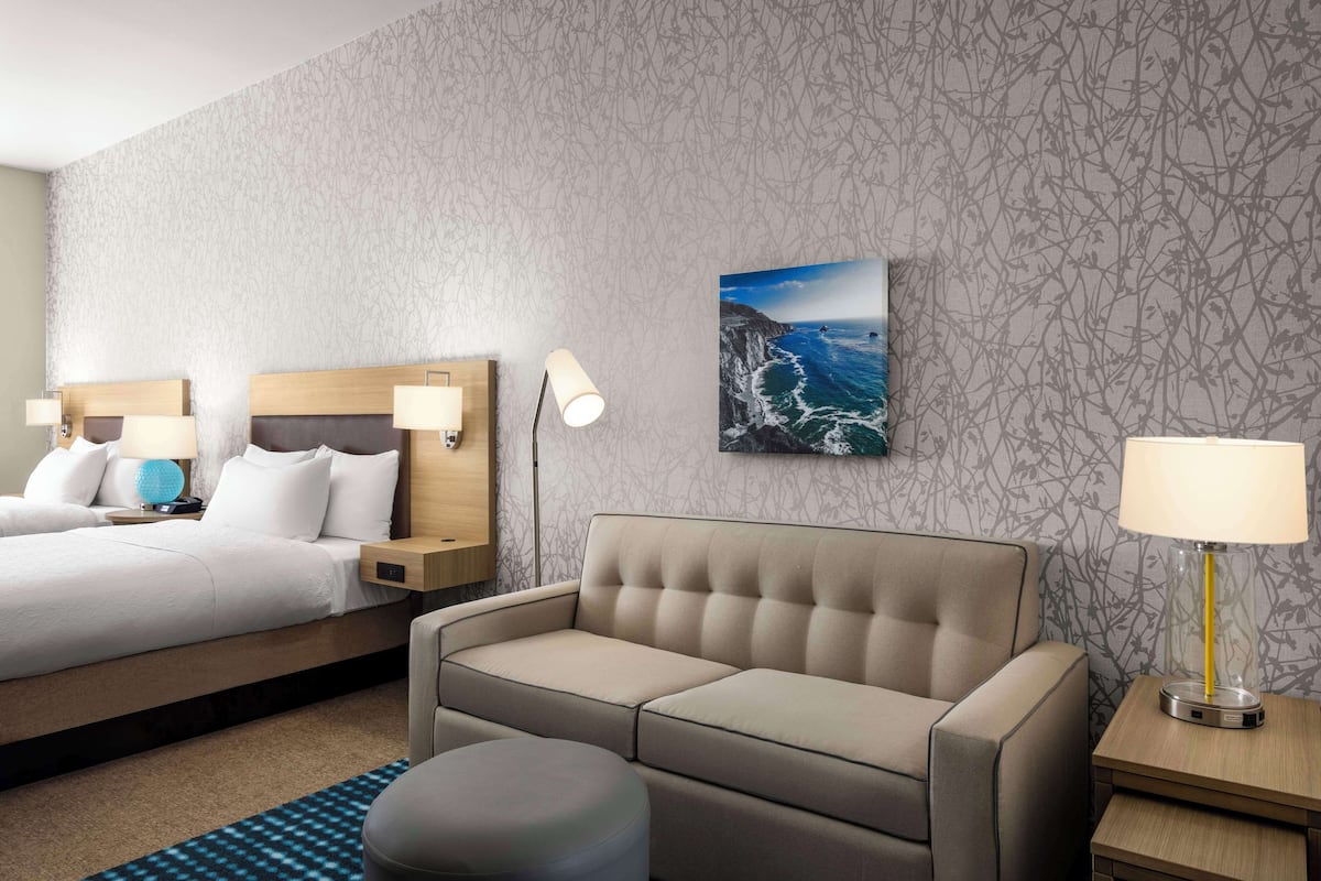 Una habitación de hotel con cama, sofá, una mesita y una lámpara.