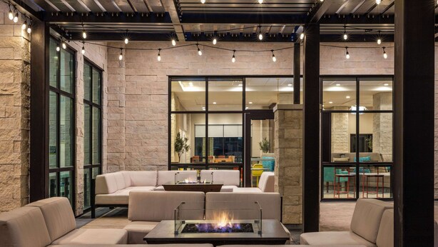 Un área de estar exterior moderna con una chimenea, muros de piedra y ventanas amplias.
