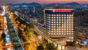 Een hoog gebouw met een opvallend "Hilton Garden Inn" bord, omgeven door een stadsgezicht met zichtbare wegen en verafgelegen bergen.