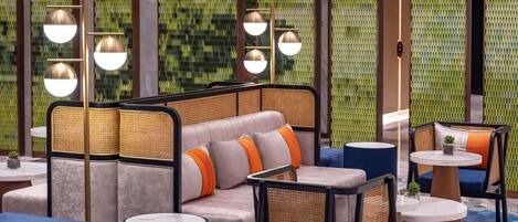 A modern lounge area with a sofa, chairs, and tables, featuring a patterned wall and pendant lighting.
