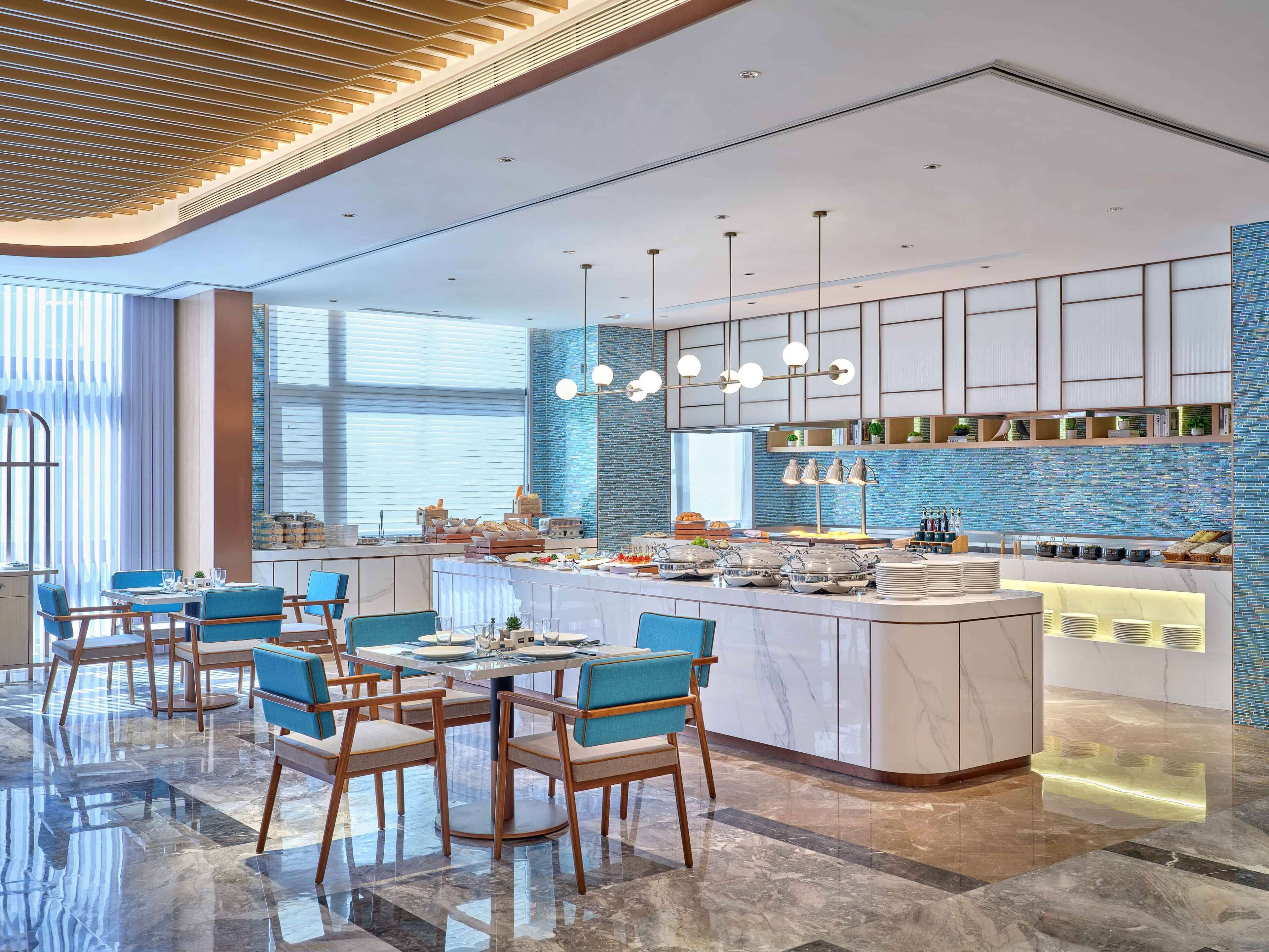 Eine moderne Hotellobby mit einer zentralen Insellounge, einer Sitzgruppe und einer blauen Fliesenwand.