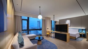 Een moderne hotelkamer met een bank, een bureau met een flatscreen-televisie, een bed en een groot raam met uitzicht op de stad.