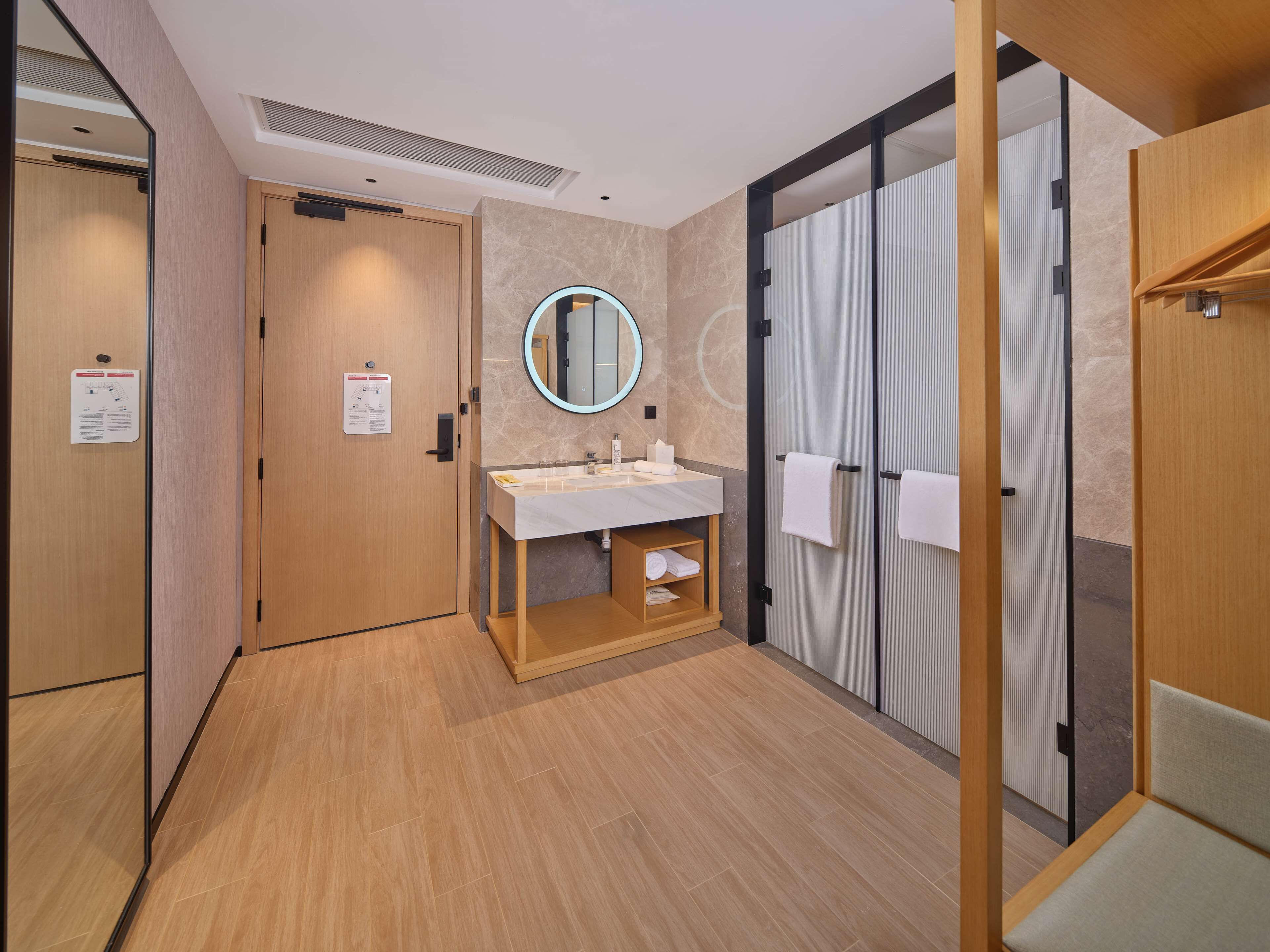 A modern bathroom with a wooden vanity, a round mirror, and a towel rack.