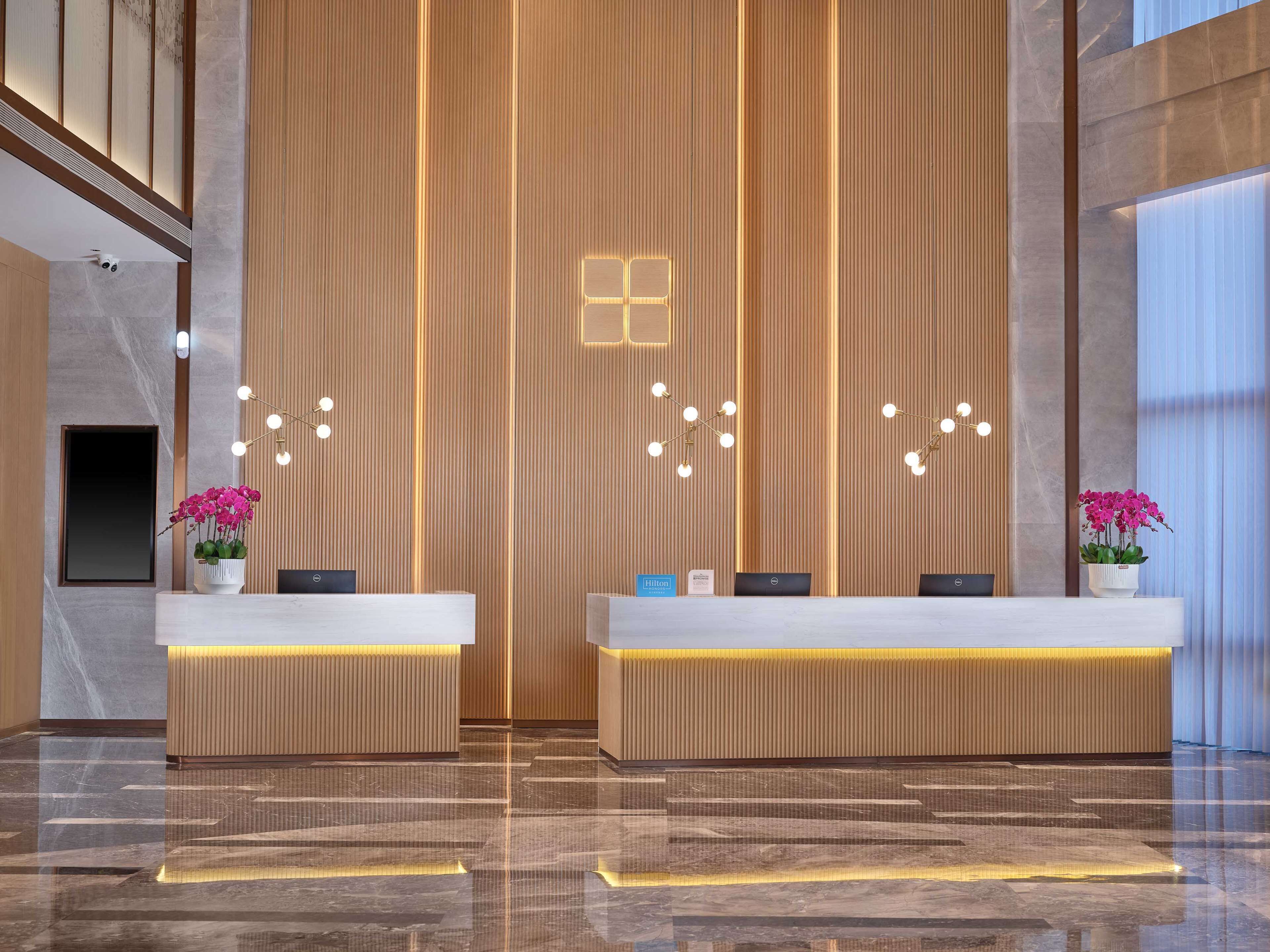 A modern hotel reception area with two reception desks, a vertical wooden panel wall, and a polished marble floor.