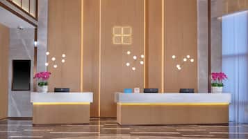 A modern hotel reception area with two reception desks, a vertical wooden panel wall, and a polished marble floor.