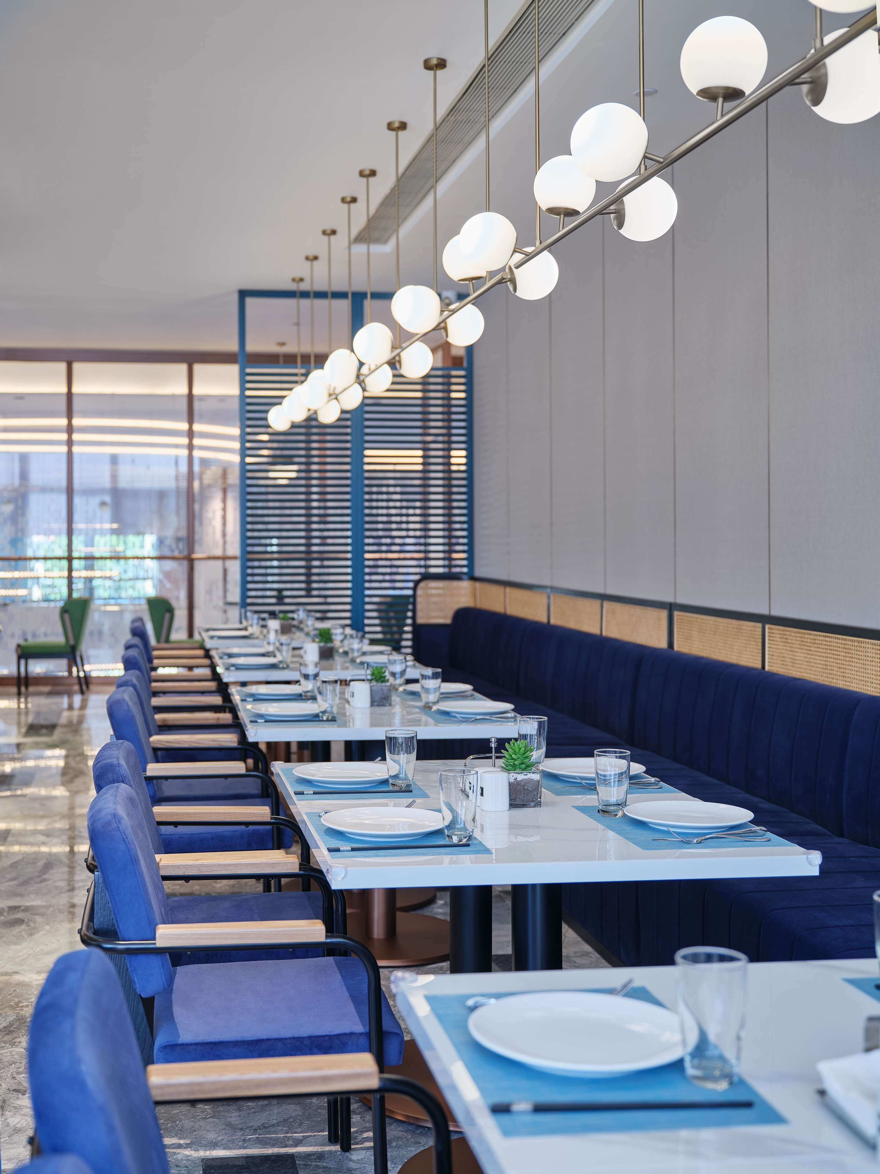 A modern restaurant with long tables, blue chairs, and a blue booth.
