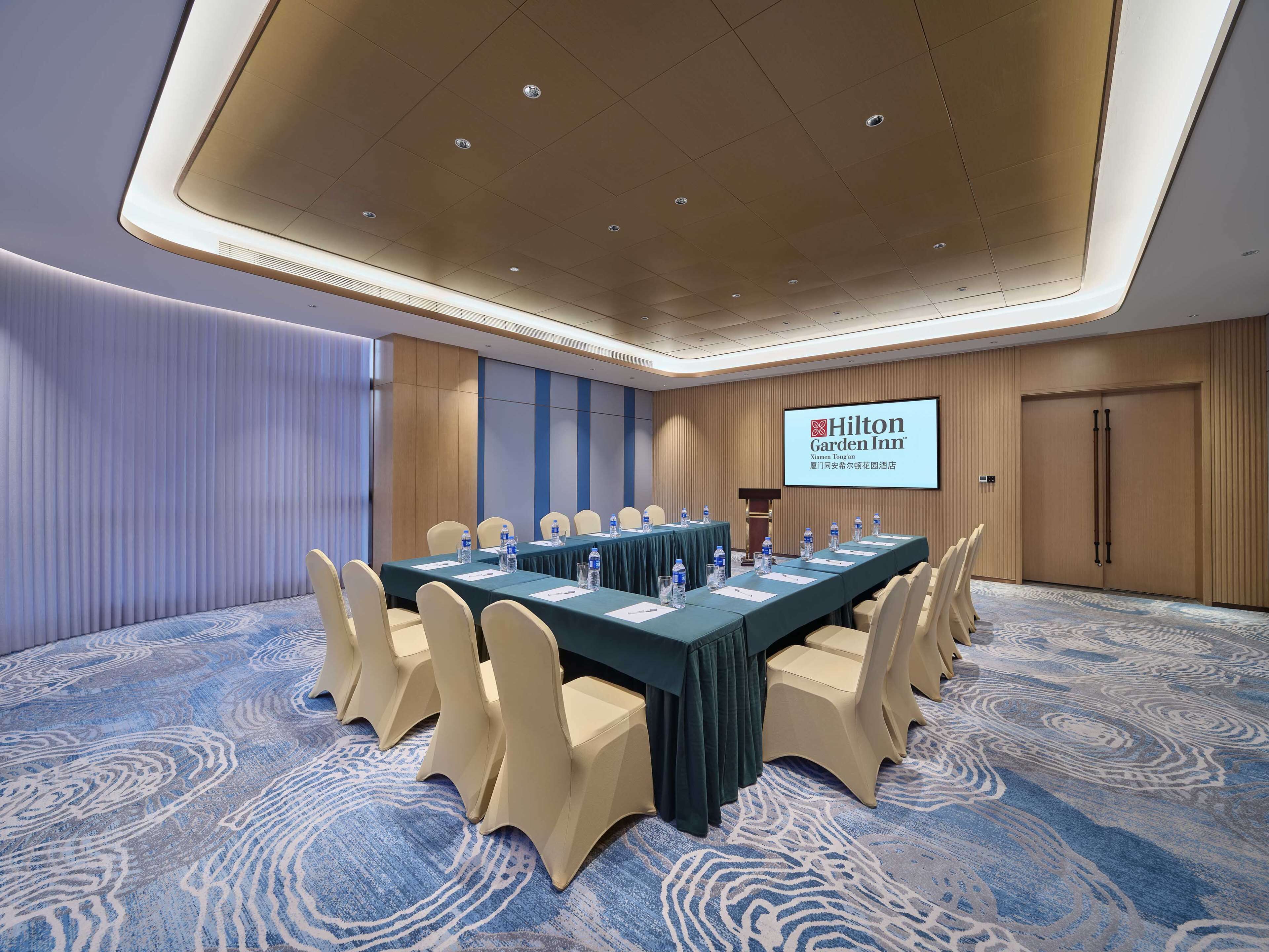 A conference room with a long table, beige chairs, and a blue carpet.