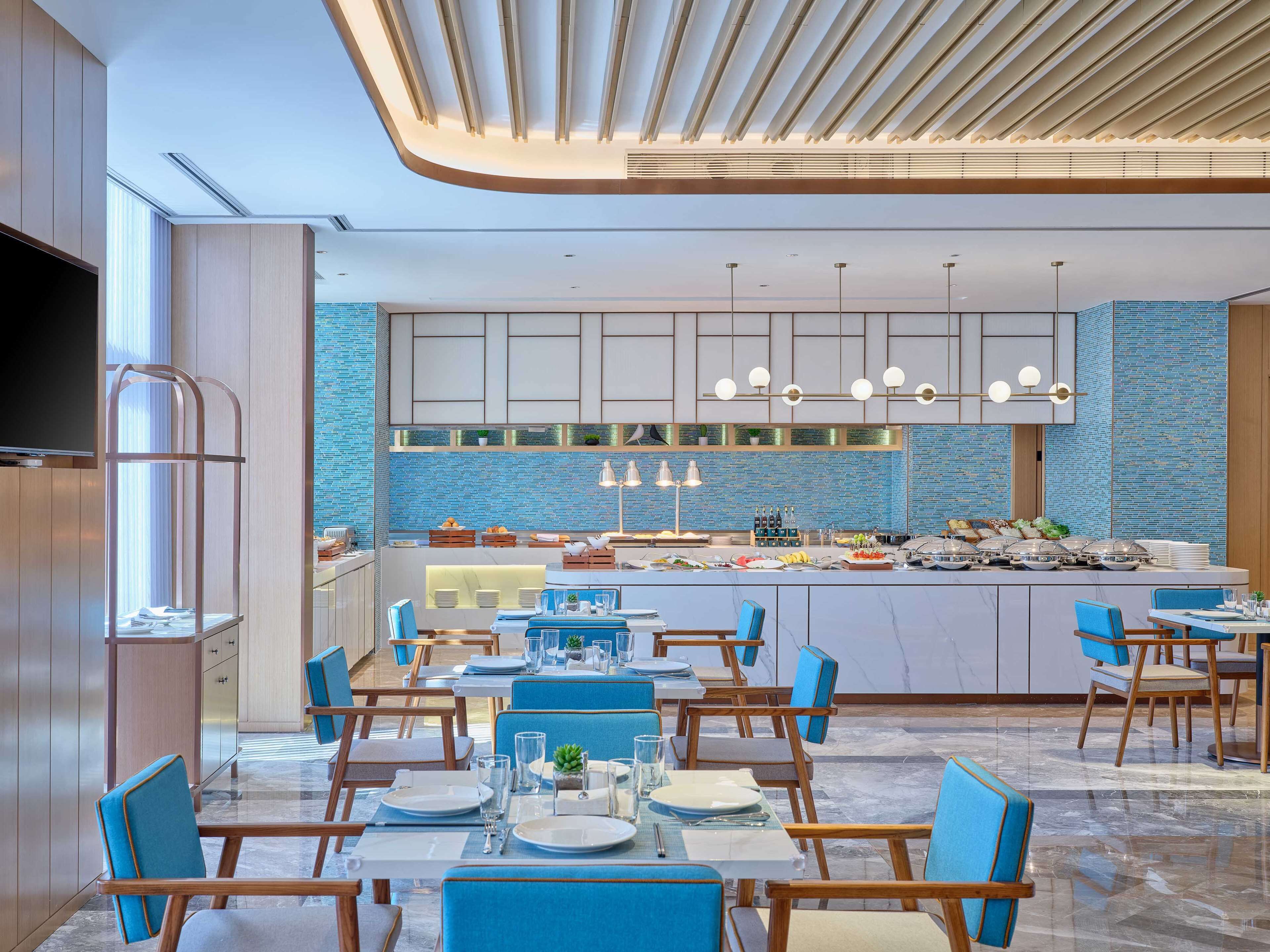 Un comedor moderno con una isla central, sillas azules y una cocina al fondo.