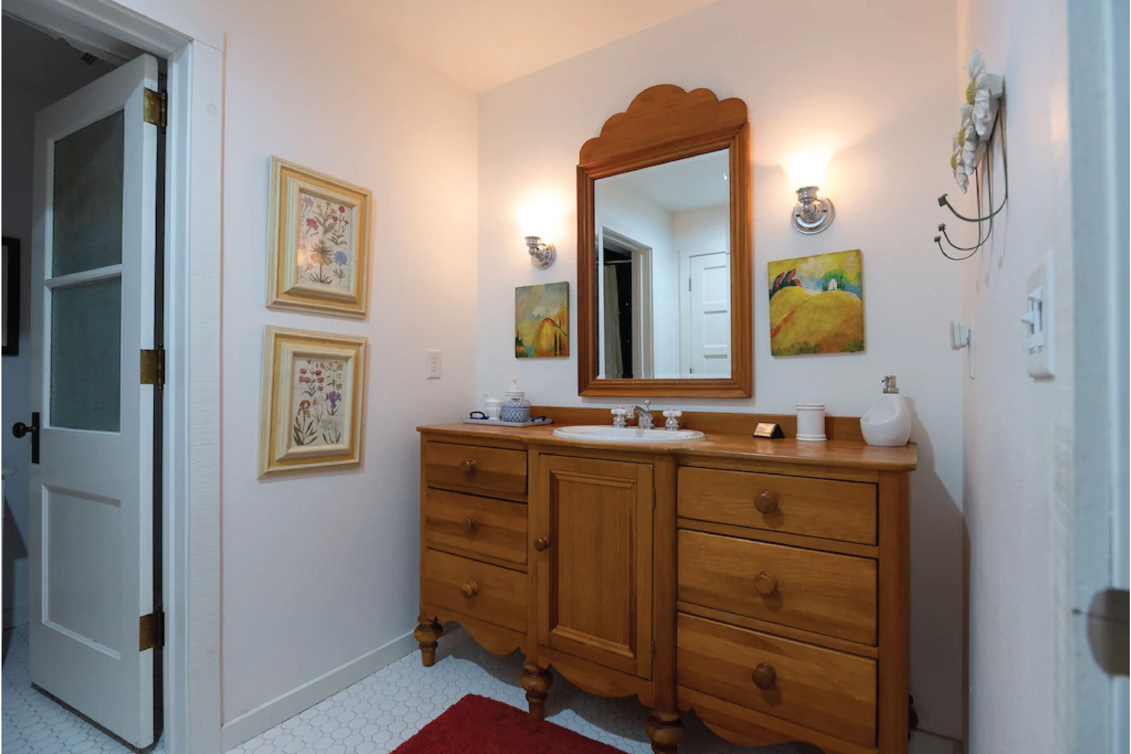 A bathroom with a wooden vanity, a large mirror, and three framed artworks on the wall.