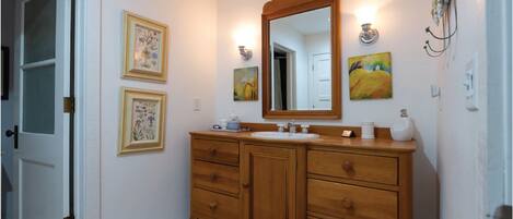A bathroom with a wooden vanity, a large mirror, and three framed artworks on the wall.
