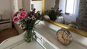 Een kamer met een witte ladekast, een bloemenvaas, een spiegel en een klok.