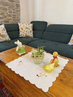 Une table basse en bois sur laquelle repose un chemin de table en dentelle blanche, une figurine de lapin en céramique, une statuette d’oiseau, une petite plante et une figurine de canard jaune.