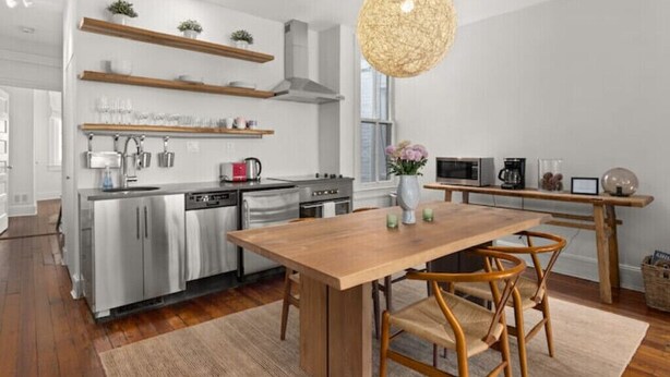 A modern kitchen with stainless steel appliances, wooden shelves, and a dining area with a wooden table and chairs.