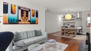 A modern living room with a grey sofa, a dining area with a wooden table, and a kitchen in the background.