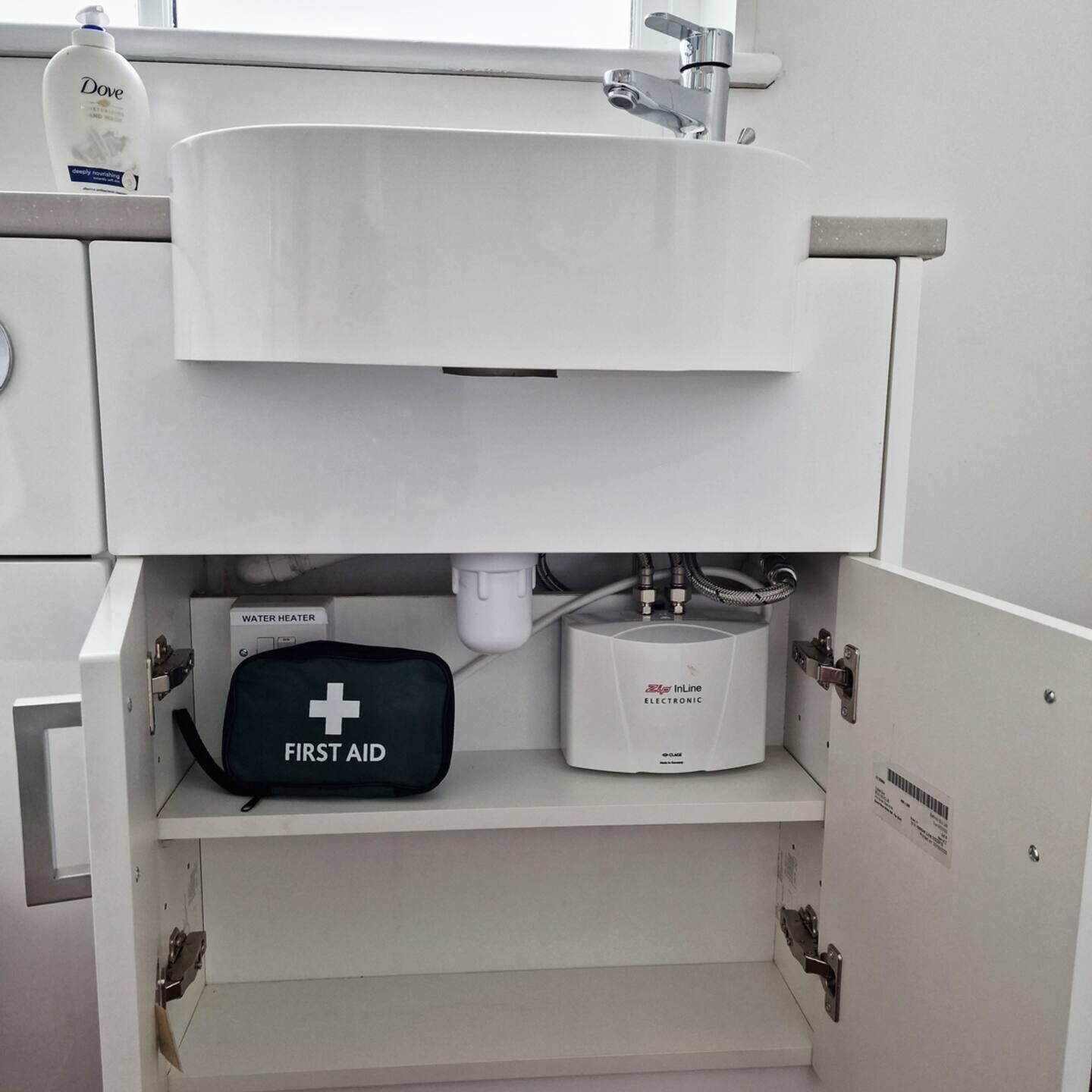 Une salle de bain avec un lavabo blanc, une trousse de premiers secours et un chauffe-eau.