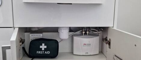 Une salle de bain avec un lavabo blanc, une trousse de premiers secours et un chauffe-eau.