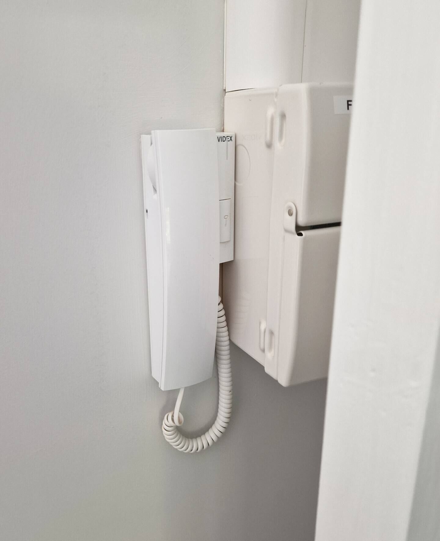 A white telephone mounted on a wall next to a white appliance, possibly a refrigerator.