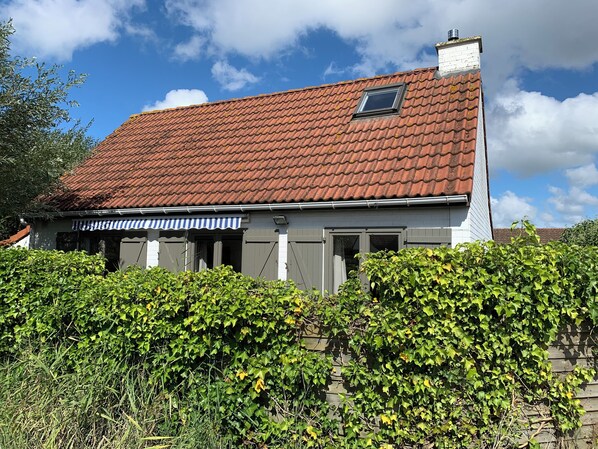 Une maison avec un toit recouvert de tuiles rouges, des murs gris et une petite fenêtre.
