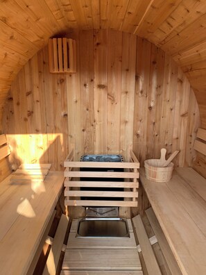 A sauna with wooden walls and benches, a metal bench, and a wooden bucket with a spoon.