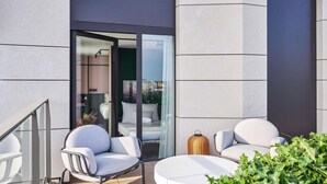 A modern outdoor seating area with two white chairs and a round table, a wicker lamp, and a glass door leading to an interior space.