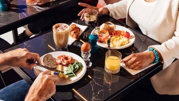 Un gruppo di persone che consuma un pasto a tavola, con diversi prodotti per la colazione, tra cui croissant, uova e pane tostato.
