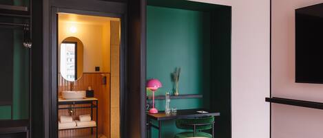 Une chambre d’hôtel moderne comprenant un lit, un bureau avec une chaise, une petite table avec une lampe et un miroir.