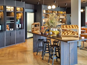 A modern café interior with a central bar area, wooden stools, and a variety of baked goods displayed on the counter.
