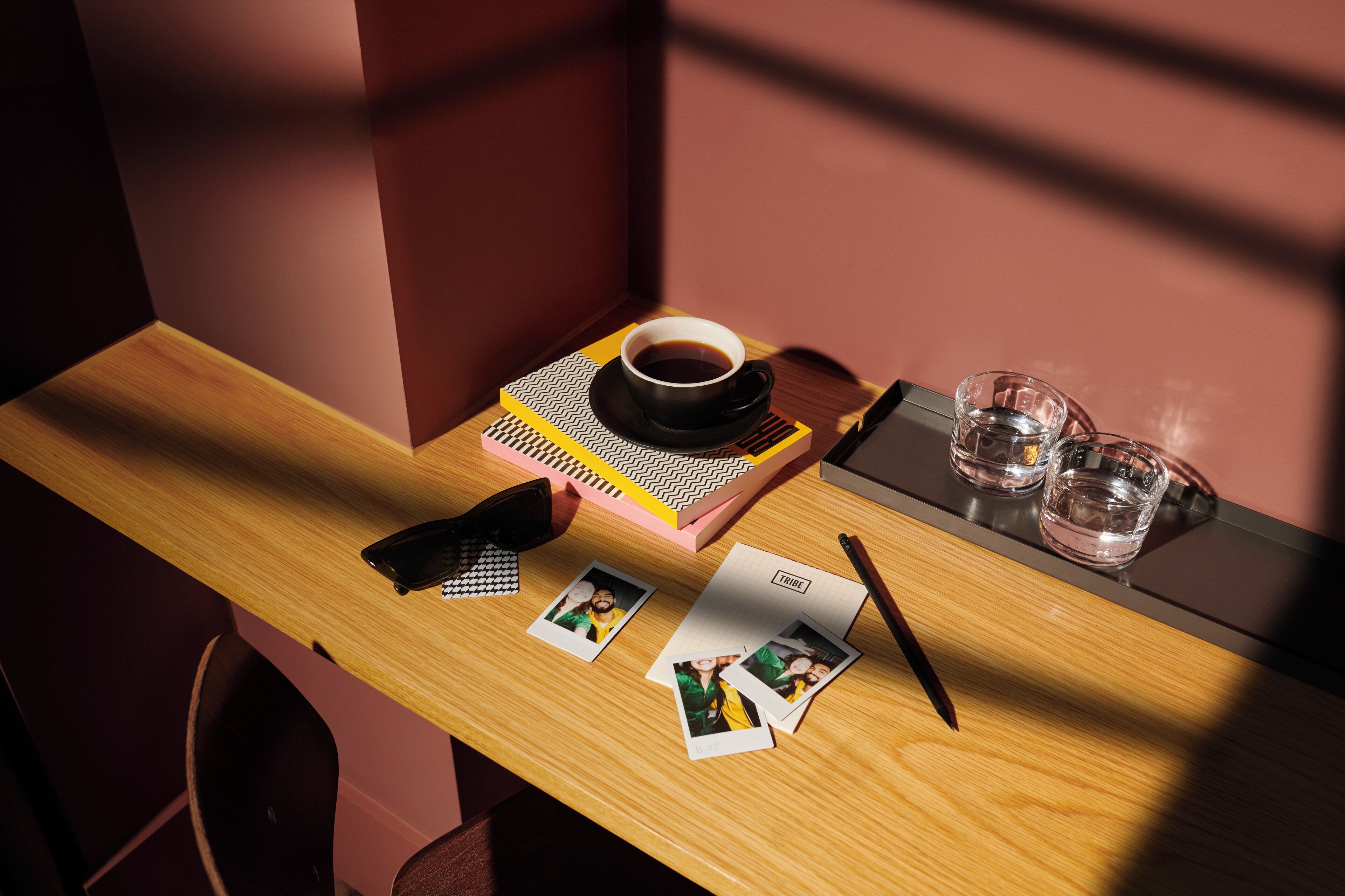 Un bureau en bois avec une tasse de café, un carnet, deux verres et quelques photographies.