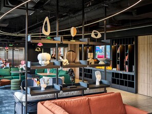 A modern interior with a suspended shelf holding various decorative items, a seating area with a red sofa, and a television in the background.